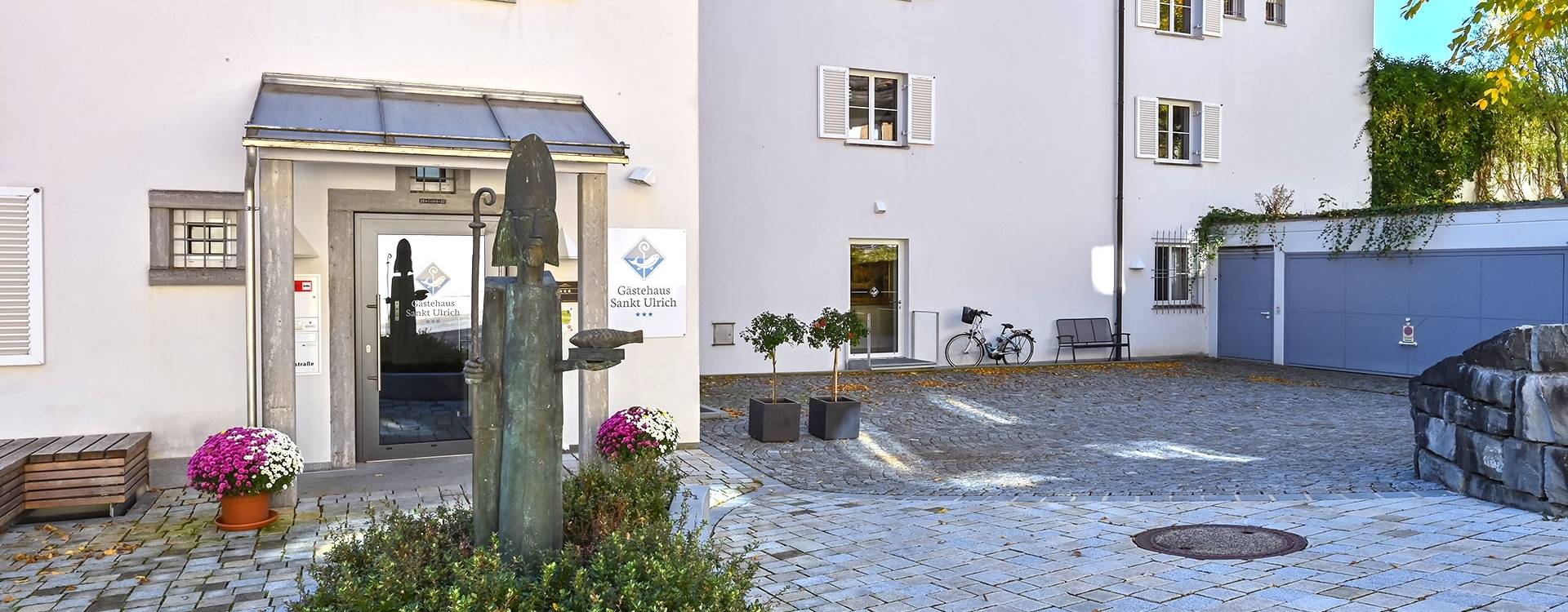 Eingang des Gästehauses Sankt Ulrich mit Statue, Pflanzkübeln und Fahrrad im Hof.