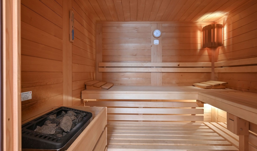 Holzsauna mit Gästehaus Sankt Ulrich mit Sitzbänken, Saunasteinen links und einer Wanduhr an der Rückwand.