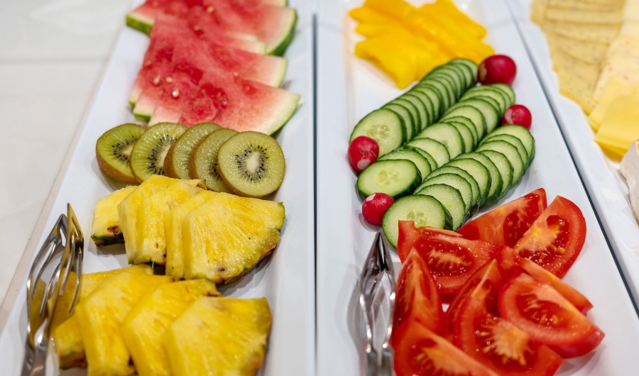 Verschiedene frische Obst- und Gemüsescheiben auf weißen Tellern, darunter Wassermelone, Kiwi, Ananas, Gurke, Tomate und Radieschen.