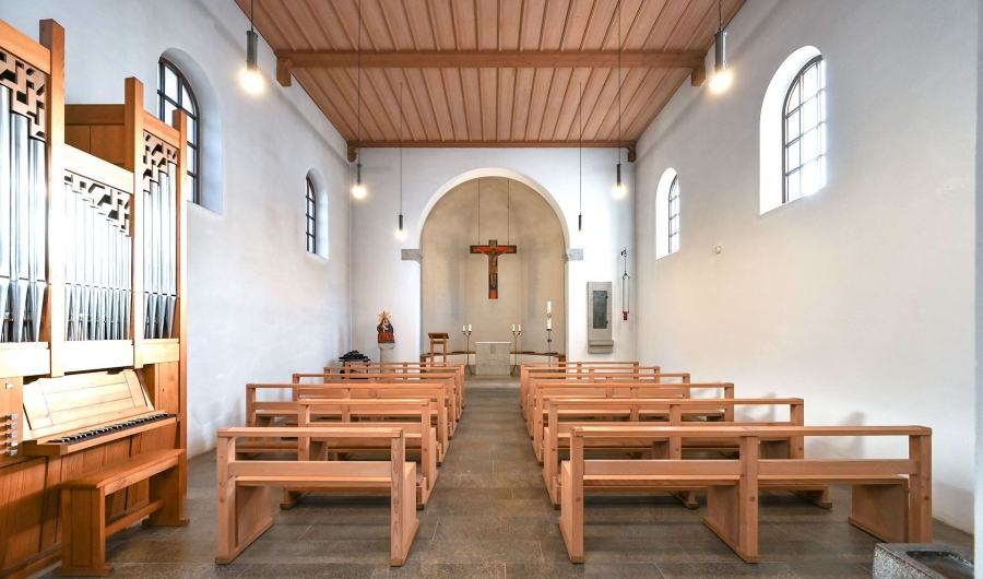 Innenraum der hauseigenen Kapelle St. Max mit Holzdecken, hölzernen Kirchenbänken, einer Orgel links und einem Kreuz an der Altarwand.