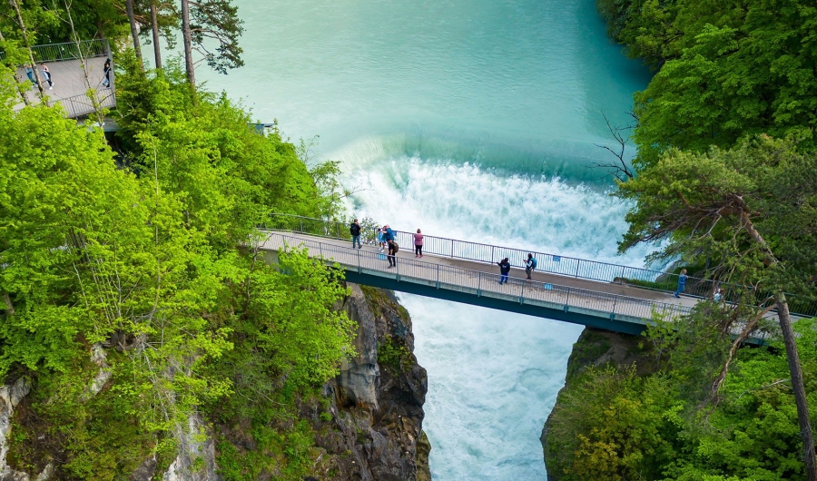 Die Brücke ‚Maxsteg‘ mit mehreren Menschen auf der Brücke über dem Lechfall mit türkisfarbenem Wasser, umgeben von dichtem grünem Wald.